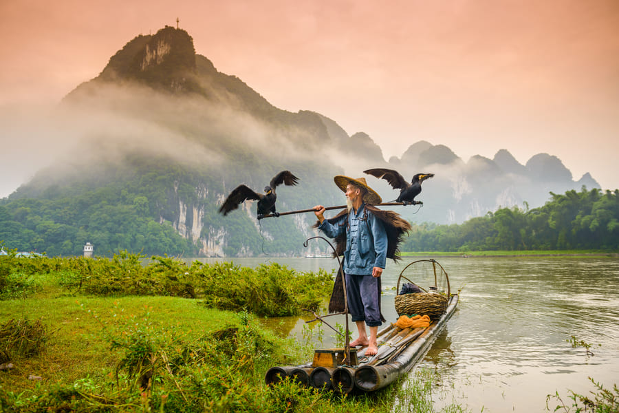 Pescador de cormorán sobre una lancha en el río Yulong en Yangshuo con montañas al fondo expertos en viajes a China en un templo tradicional