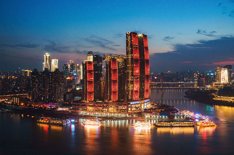 El icónico Raffles City Chongqing Itinerarios Personalizadosbrillando durante la noche. Una postal impresionante de la arquitectura futurista y el desarrollo urbano en el corazón de China.Itinerarios Personalizados